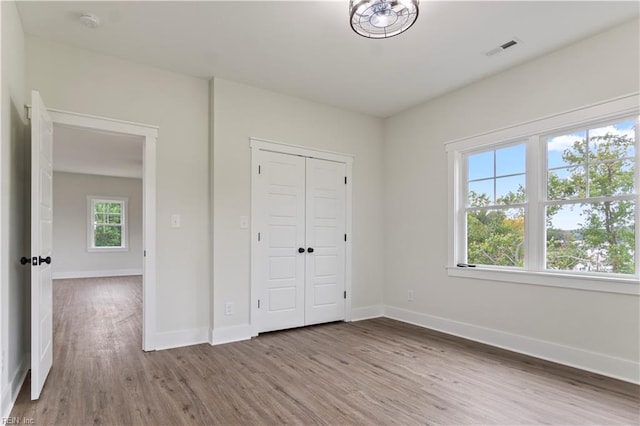 unfurnished bedroom with a closet, hardwood / wood-style floors, and multiple windows