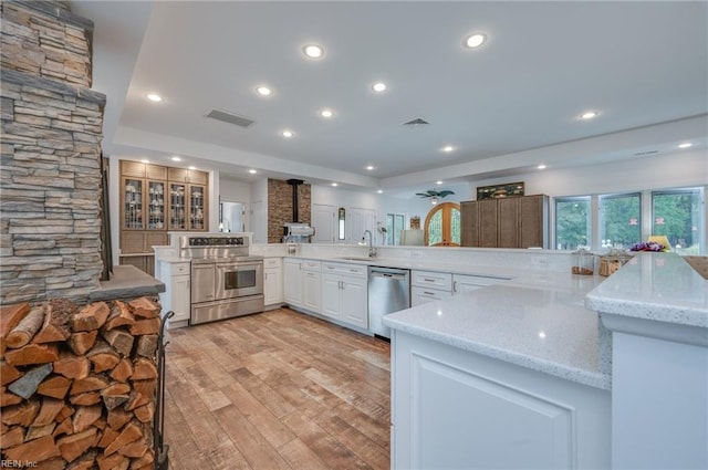 kitchen with light stone counters, white cabinetry, stainless steel appliances, kitchen peninsula, and light wood-type flooring