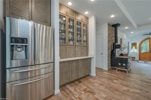 kitchen with a wood stove, ceiling fan, vaulted ceiling, stainless steel refrigerator with ice dispenser, and hardwood / wood-style flooring