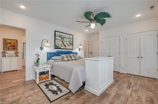 bedroom featuring two closets, ceiling fan, and light hardwood / wood-style flooring