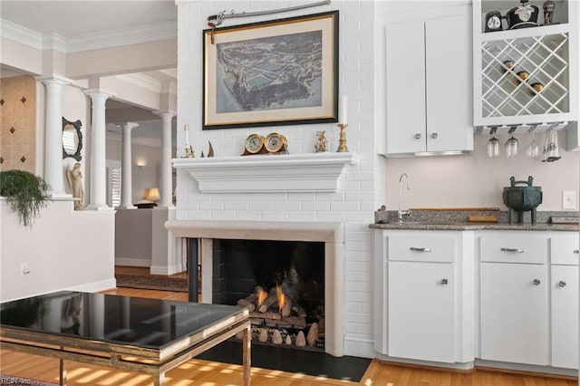 interior space featuring ornamental molding, light wood-type flooring, a fireplace, and decorative columns