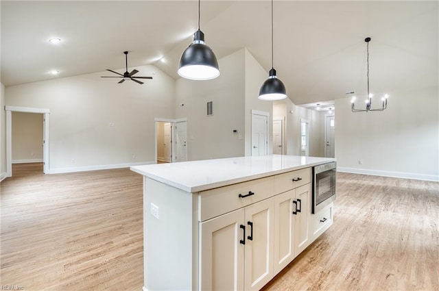 kitchen with pendant lighting, white cabinetry, stainless steel microwave, and light hardwood / wood-style flooring