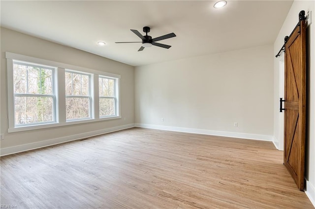 spare room with ceiling fan, a barn door, and light wood-type flooring