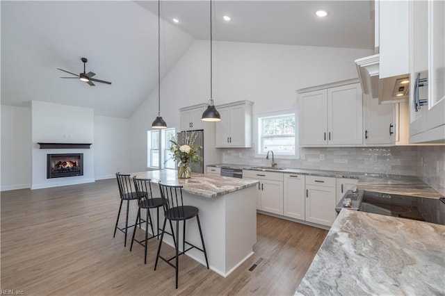 kitchen with sink, a kitchen island, white cabinets, and high vaulted ceiling