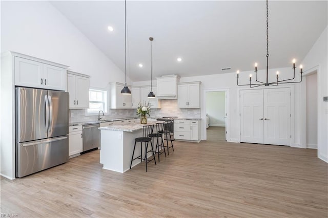 kitchen featuring stainless steel appliances, decorative light fixtures, a breakfast bar, a kitchen island, and light wood-type flooring