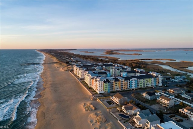 aerial view at dusk featuring a water view and a beach view