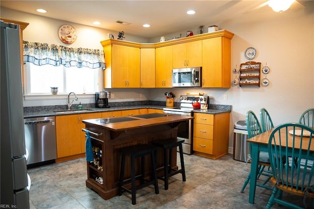 kitchen with appliances with stainless steel finishes, sink, a kitchen bar, and light tile floors