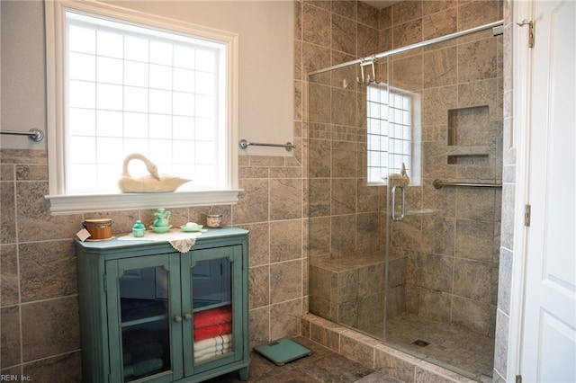 bathroom featuring tile flooring, a shower with shower door, a healthy amount of sunlight, and tile walls