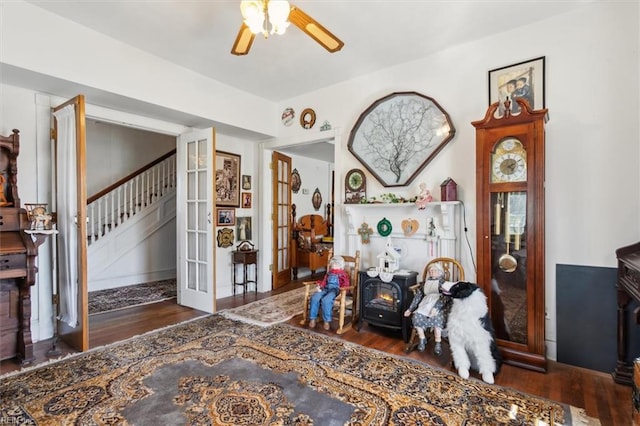 sitting room featuring french doors, ceiling fan, dark wood-type flooring, and a wood stove