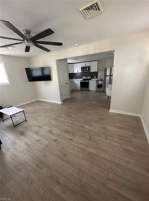 unfurnished living room featuring hardwood / wood-style floors, ceiling fan, and washer / clothes dryer