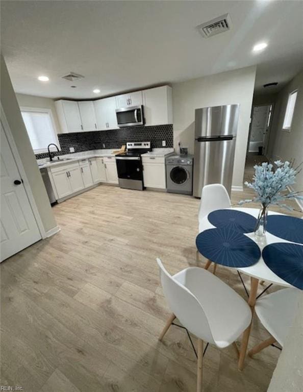 kitchen featuring light wood-type flooring, white cabinetry, stainless steel appliances, and washer / clothes dryer