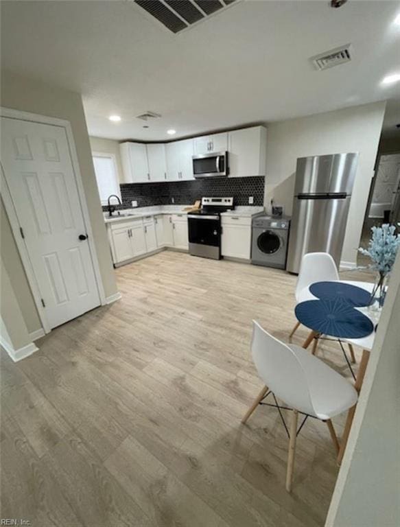 kitchen featuring stainless steel appliances, washer / dryer, tasteful backsplash, white cabinets, and light wood-type flooring