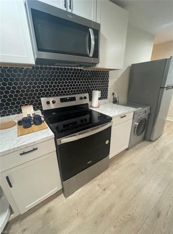 kitchen with white cabinets, backsplash, light wood-type flooring, washer / dryer, and stainless steel appliances