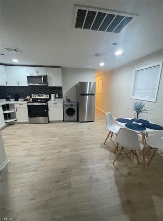 kitchen featuring light hardwood / wood-style flooring, white cabinetry, backsplash, appliances with stainless steel finishes, and washer / dryer