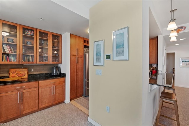 kitchen with decorative light fixtures, a breakfast bar, dark stone counters, stainless steel refrigerator, and light colored carpet