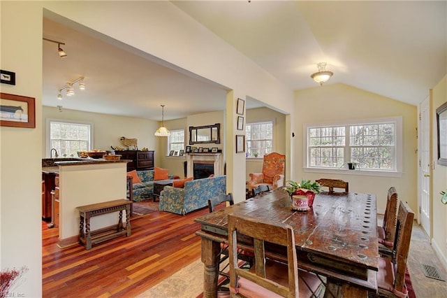 dining room with plenty of natural light, hardwood / wood-style floors, track lighting, and vaulted ceiling