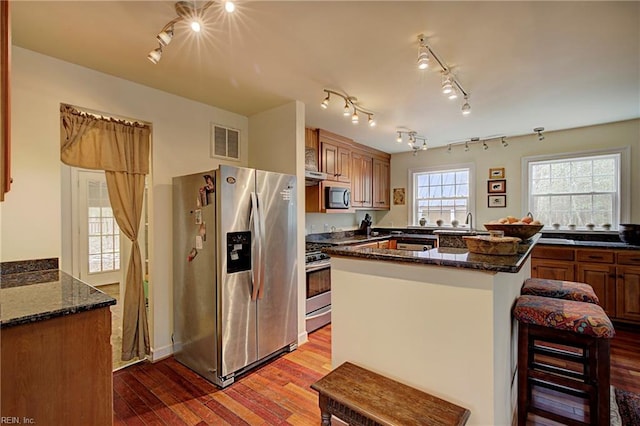 kitchen featuring rail lighting, dark stone countertops, a breakfast bar area, stainless steel appliances, and wood-type flooring