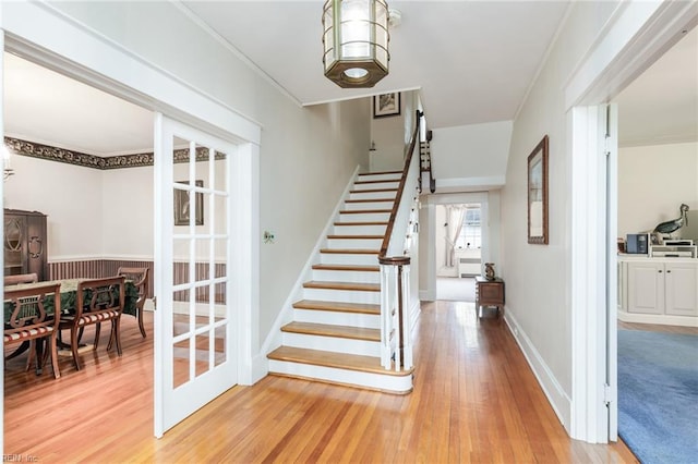 staircase with ornamental molding, light hardwood / wood-style floors, and french doors