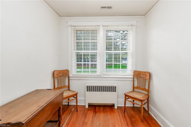 living area featuring crown molding, a healthy amount of sunlight, radiator heating unit, and hardwood / wood-style floors