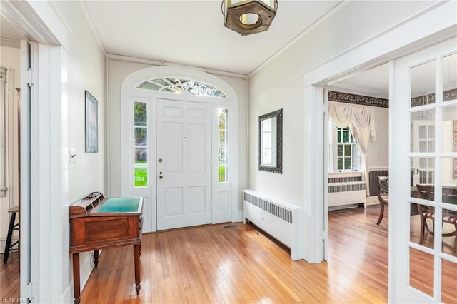 entryway with ornamental molding, radiator heating unit, and light wood-type flooring