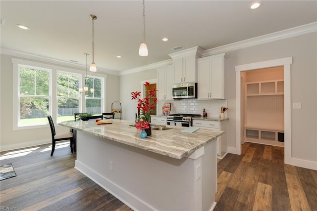 kitchen featuring appliances with stainless steel finishes, light stone counters, tasteful backsplash, an island with sink, and hanging light fixtures