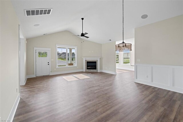 unfurnished living room with ceiling fan with notable chandelier, lofted ceiling, a wealth of natural light, and dark hardwood / wood-style flooring