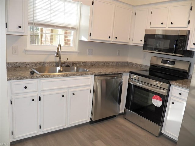 kitchen with stone countertops, stainless steel appliances, white cabinets, sink, and light wood-type flooring