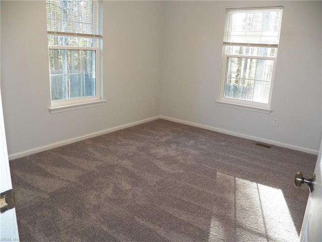 unfurnished room featuring plenty of natural light and dark carpet