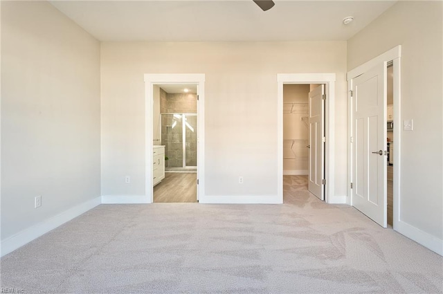 unfurnished bedroom featuring a walk in closet, connected bathroom, light colored carpet, and a closet