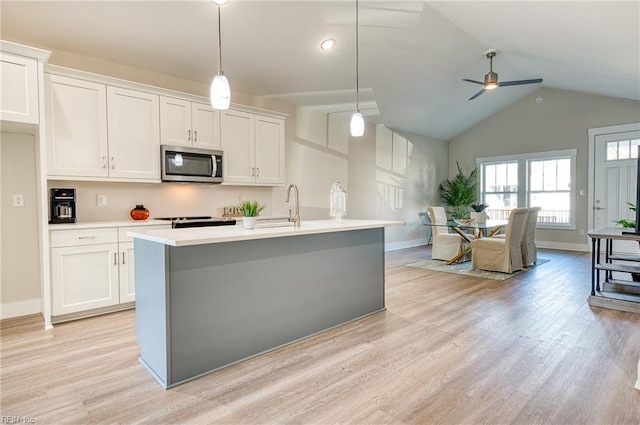 kitchen featuring vaulted ceiling, a kitchen island with sink, ceiling fan, decorative light fixtures, and white cabinetry