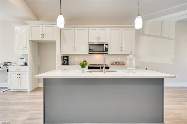 kitchen with white cabinets, decorative light fixtures, and a center island with sink