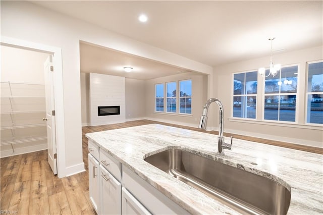 kitchen with white cabinetry, decorative light fixtures, light stone countertops, sink, and a large fireplace