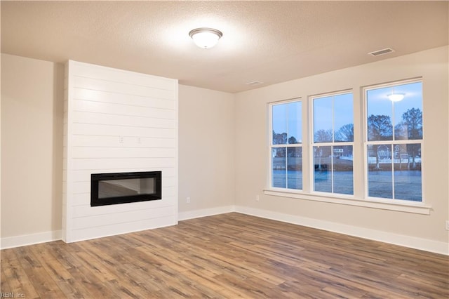 unfurnished living room featuring a fireplace, wood-type flooring, and a textured ceiling