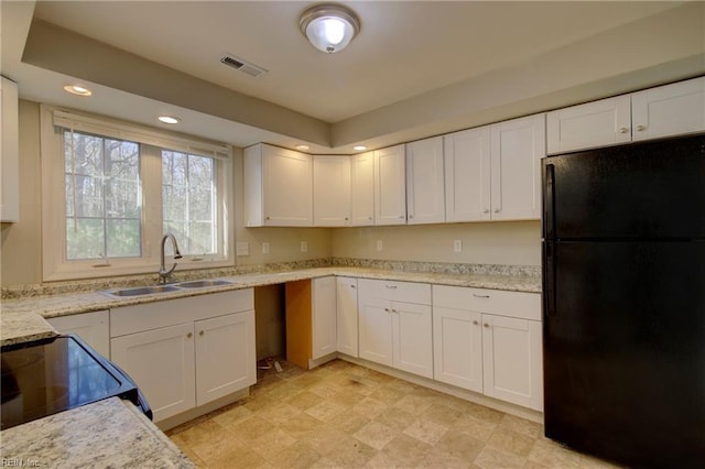 kitchen featuring white cabinets, black fridge, light stone countertops, and sink