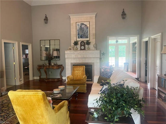 living room featuring a high ceiling, a tiled fireplace, and wood-type flooring