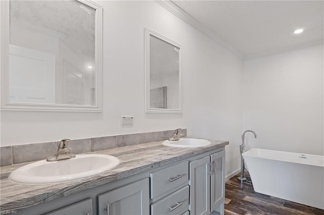 bathroom with ornamental molding, hardwood / wood-style floors, a bathing tub, and dual bowl vanity