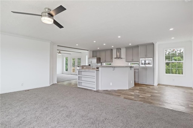 kitchen featuring wall chimney range hood, plenty of natural light, stainless steel appliances, ceiling fan, and hardwood / wood-style floors