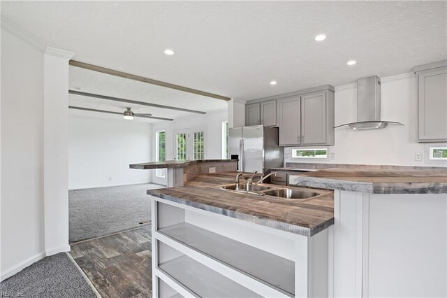 kitchen with gray cabinetry, wall chimney exhaust hood, stainless steel fridge, sink, and dark colored carpet