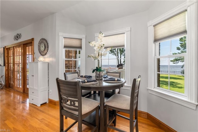 dining space with light hardwood / wood-style floors, a water view, and vaulted ceiling