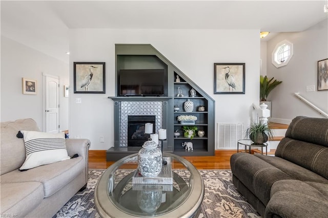 living room with a tiled fireplace, built in shelves, and hardwood / wood-style flooring