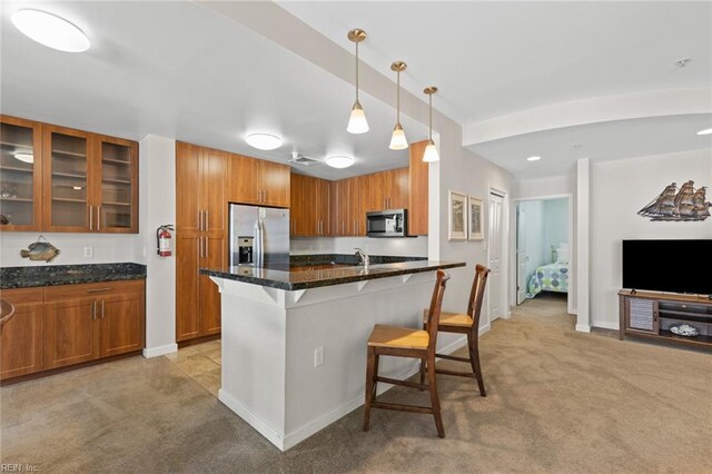 kitchen featuring dark stone counters, stainless steel appliances, hanging light fixtures, a breakfast bar area, and light colored carpet