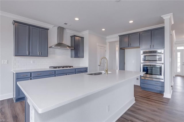 kitchen featuring sink, a kitchen island with sink, dark wood-type flooring, and wall chimney range hood