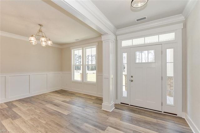 entrance foyer featuring decorative columns, light hardwood / wood-style floors, ornamental molding, and a chandelier