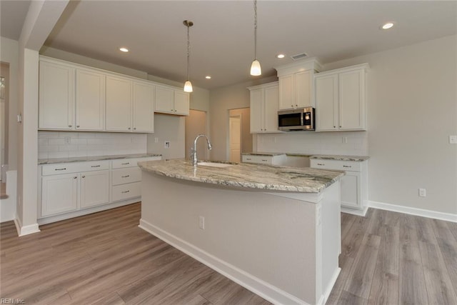 kitchen featuring sink, a center island with sink, backsplash, and white cabinetry