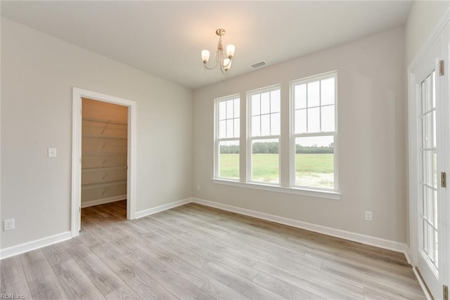 unfurnished bedroom with an inviting chandelier, a walk in closet, a closet, and light wood-type flooring