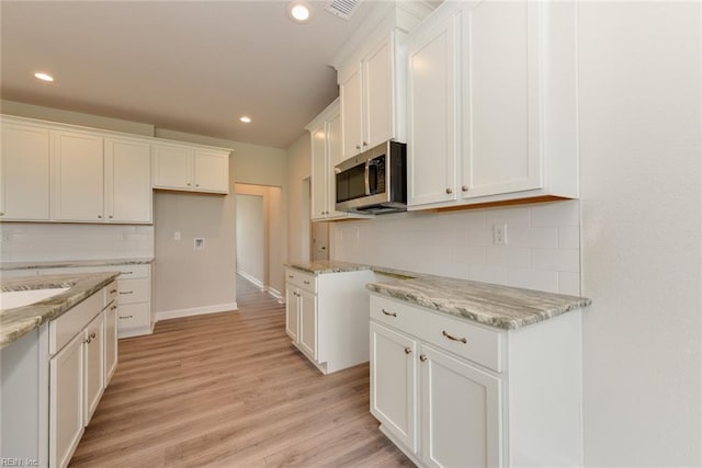 kitchen featuring white cabinetry, tasteful backsplash, light wood-type flooring, and light stone counters