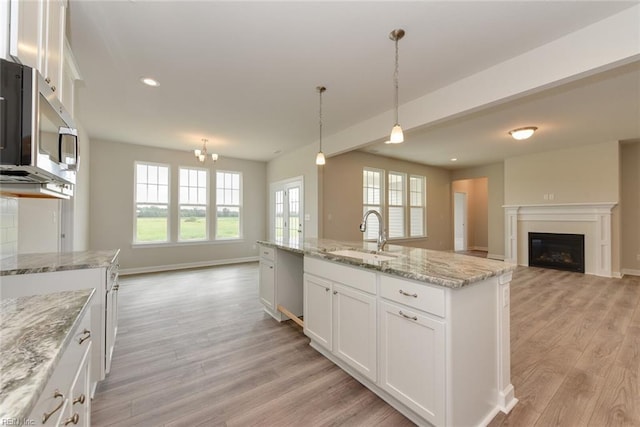 kitchen featuring light hardwood / wood-style floors, an island with sink, pendant lighting, sink, and white cabinets