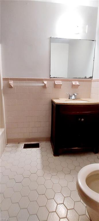 bathroom with toilet, tile flooring, vanity, and tile walls