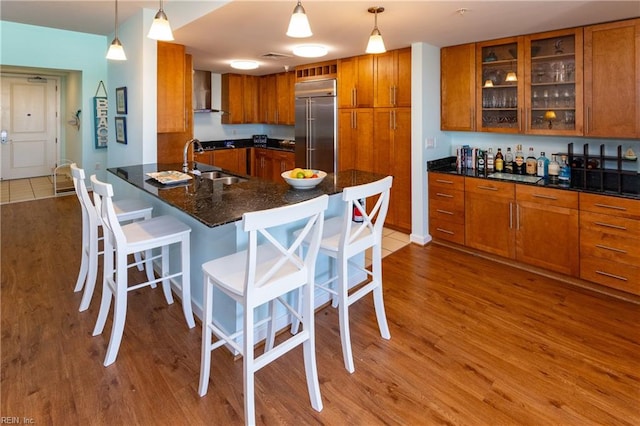 kitchen with wood-type flooring, built in fridge, wall chimney range hood, and pendant lighting