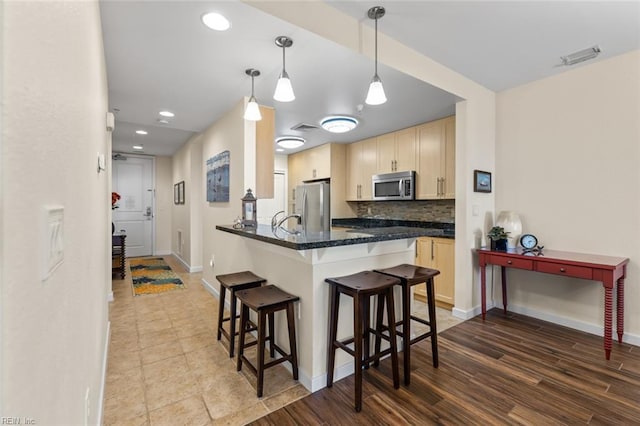 kitchen with hanging light fixtures, kitchen peninsula, decorative backsplash, a breakfast bar, and appliances with stainless steel finishes